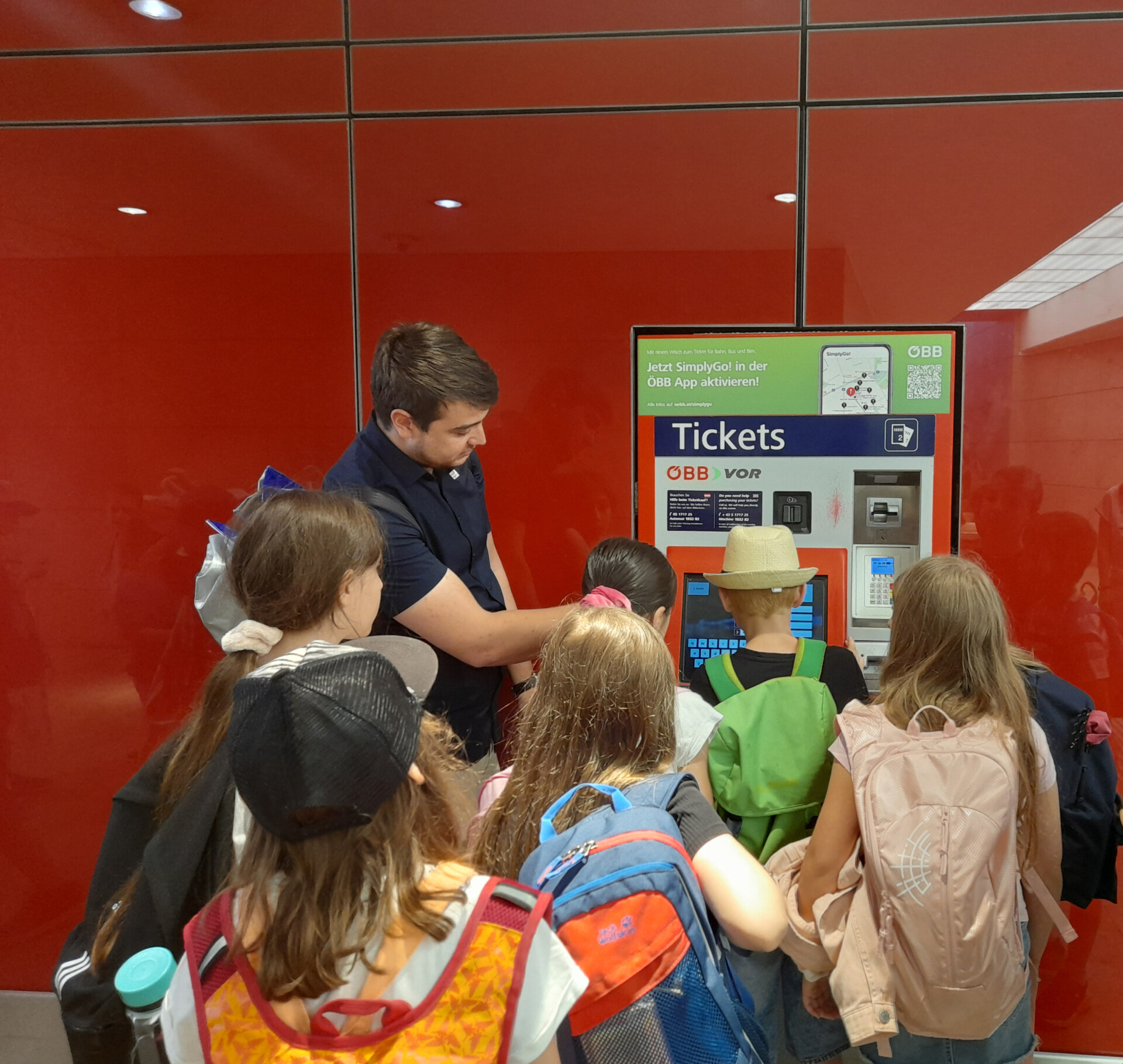 Mann erklärt Schulkindern den Fahrkartenautomaten der ÖBB