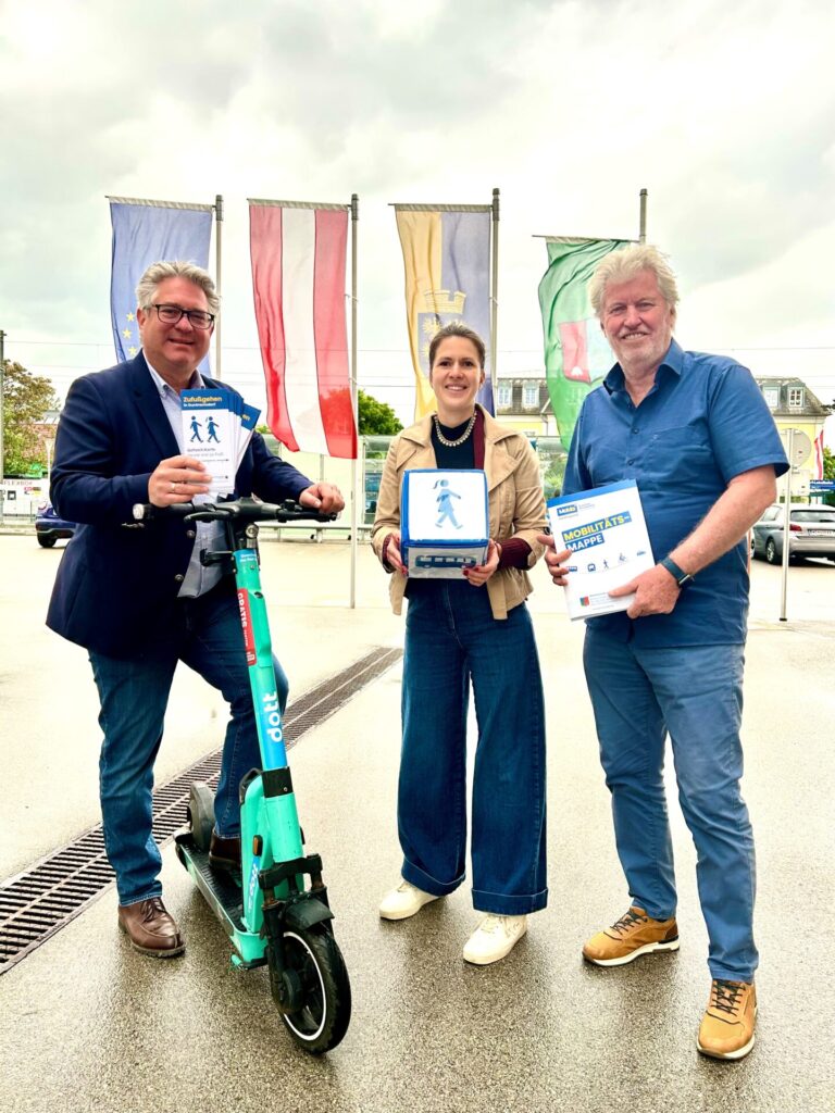 Bürgermeister, Mobilitätsmanagerin und Mobilitätsbeauftragter Guntramsdorf stehen vor Fahnen mit den Produkten Gehzeit.Karte und Mobilitätsmappe