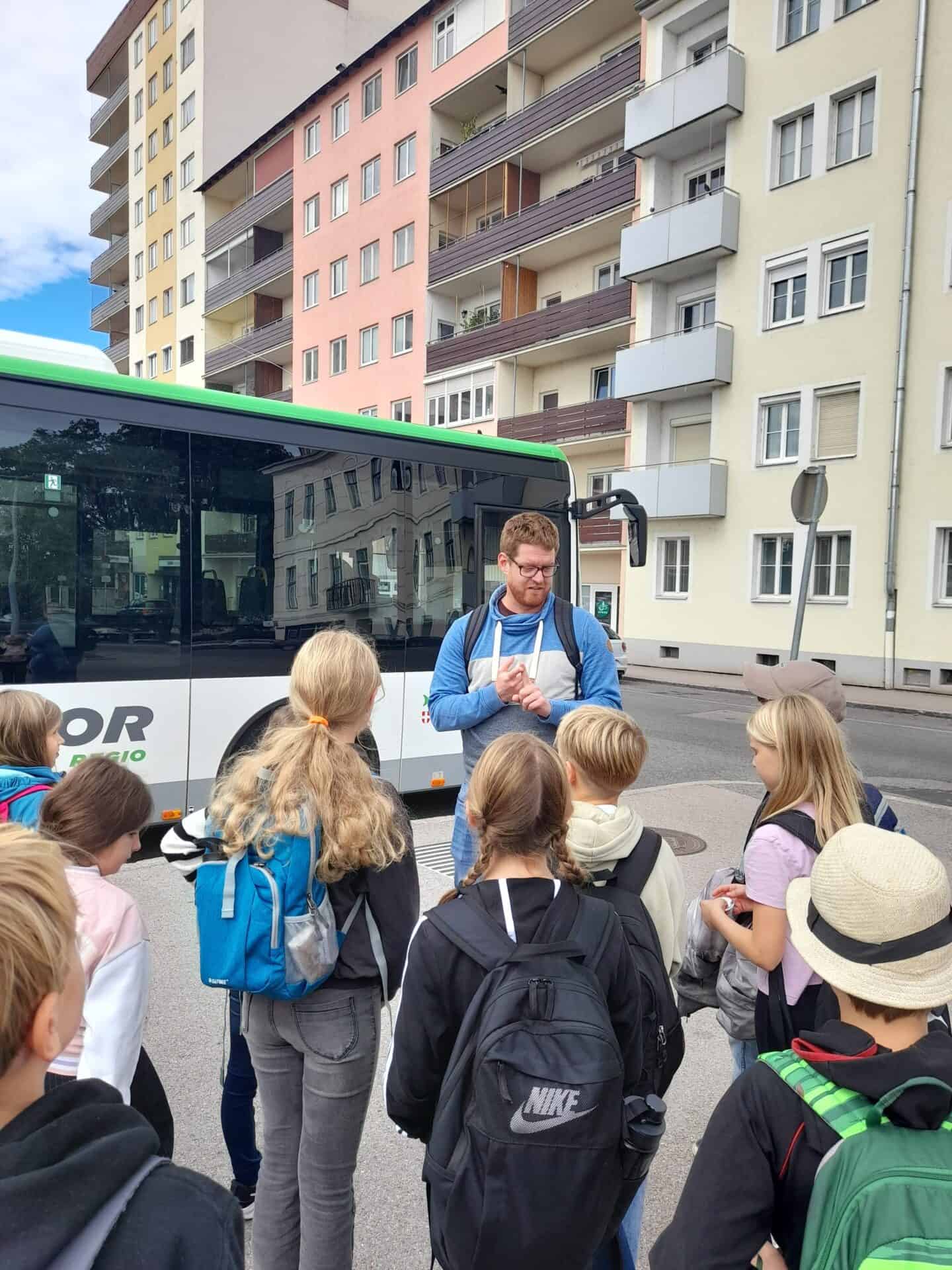NÖVOG Busplaner Dominik Karas erklärt Kindern an einer Bushaltestelle wie der Busverkehr in Niederösterreich funktioniert