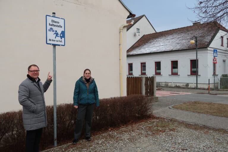 Zwei Menschen stehen auf einem Parkplatz, der als Elternhaltestelle gekennzeichnet ist.