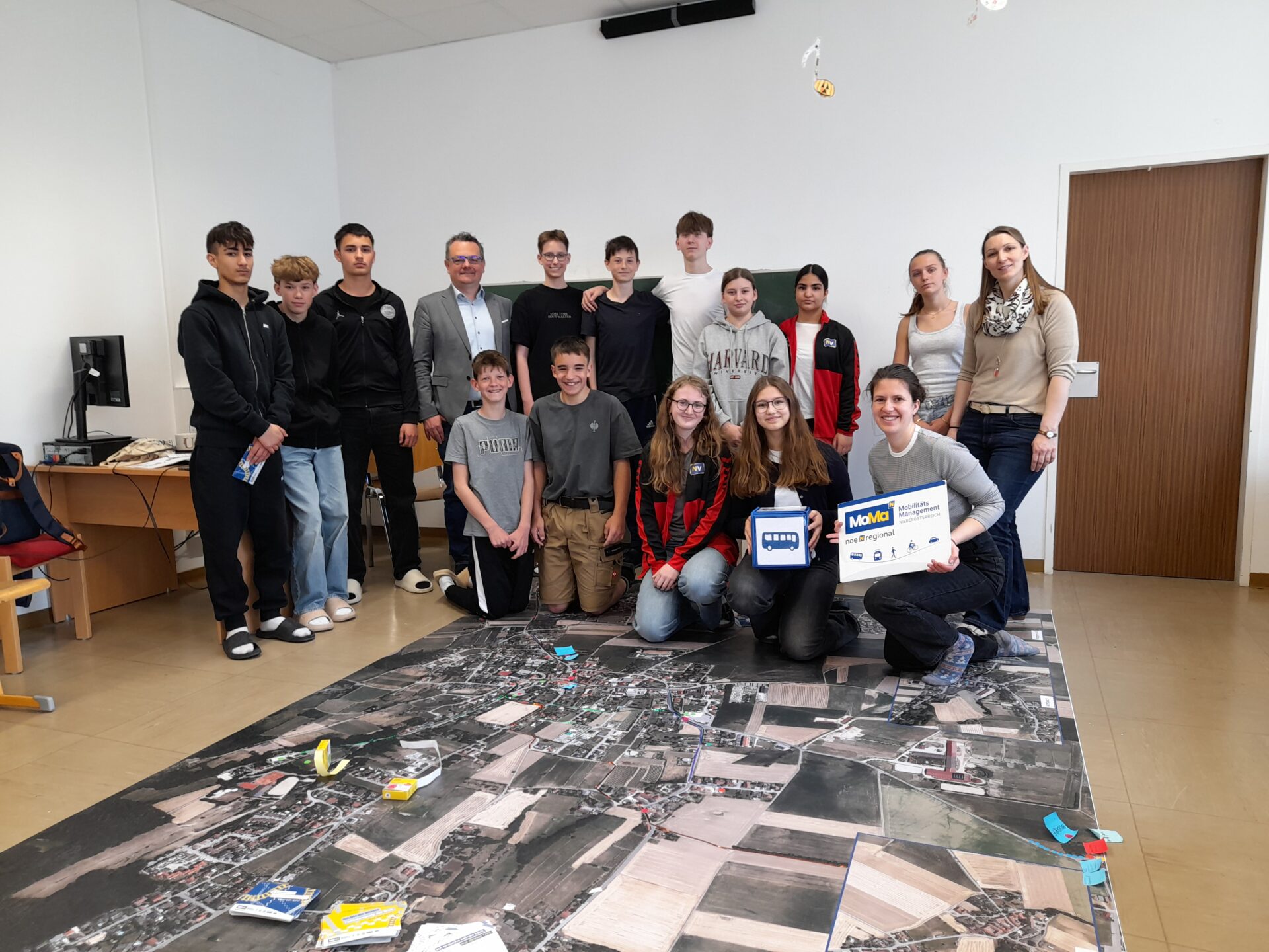 Schülerinnen und Schüler mit Gemeindepolitik vor einem großen Luftbild der Gemeinde