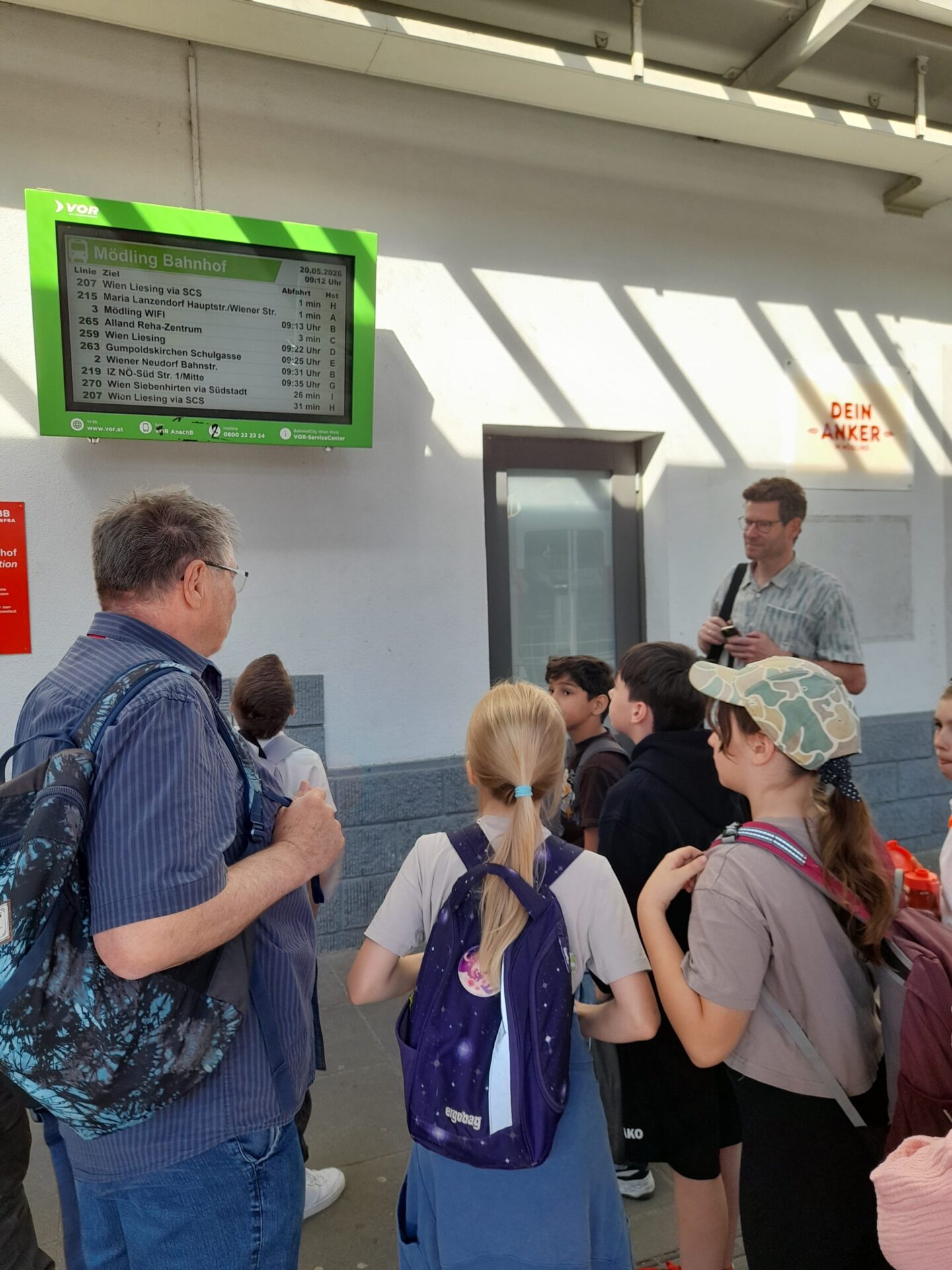 Kinder stehen vor Abfahrtsmonitor am Bahnhof
