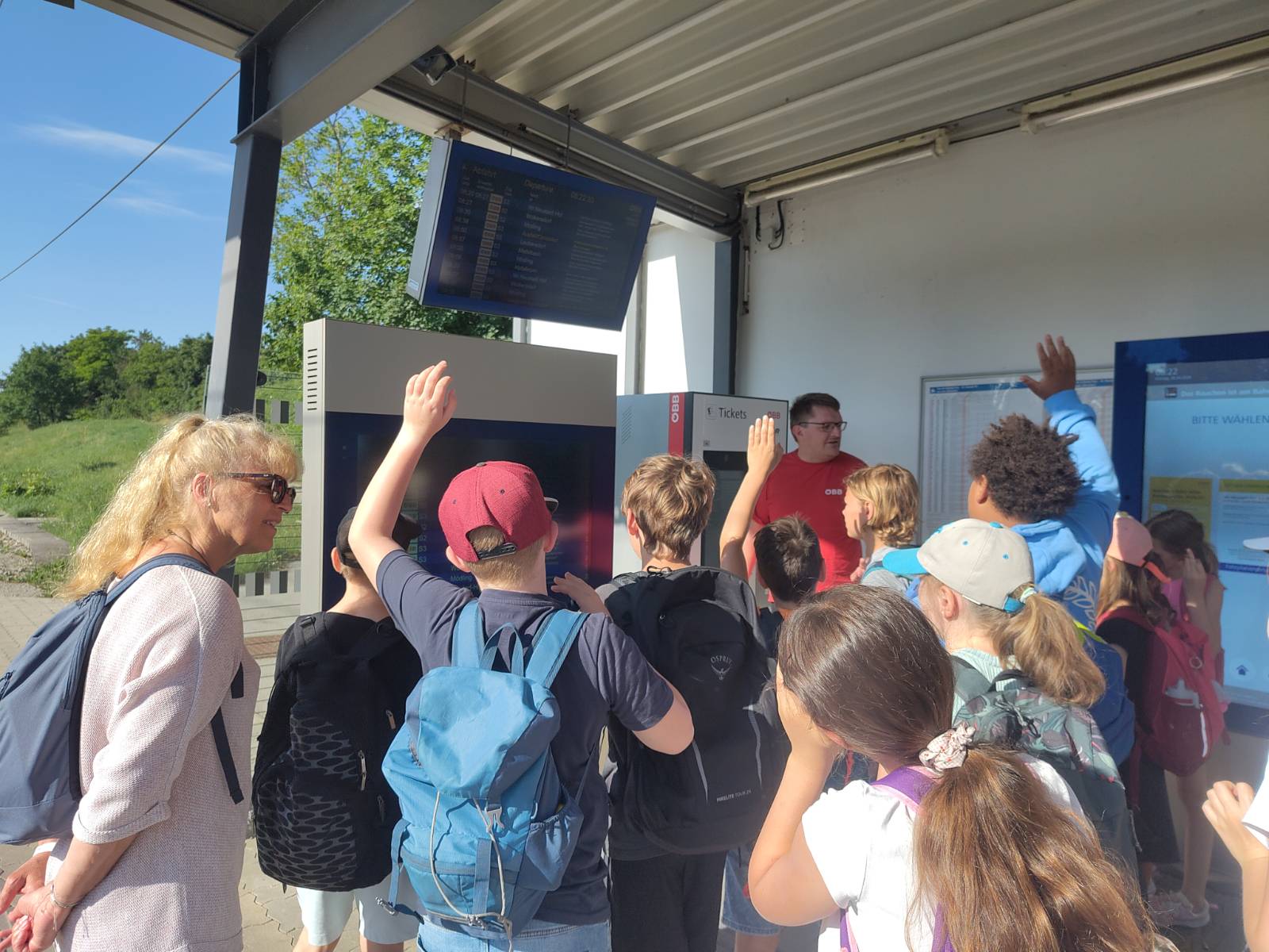 Kinder stehen an Bahnhaltestelle und lernen über die Anzeigetafel
